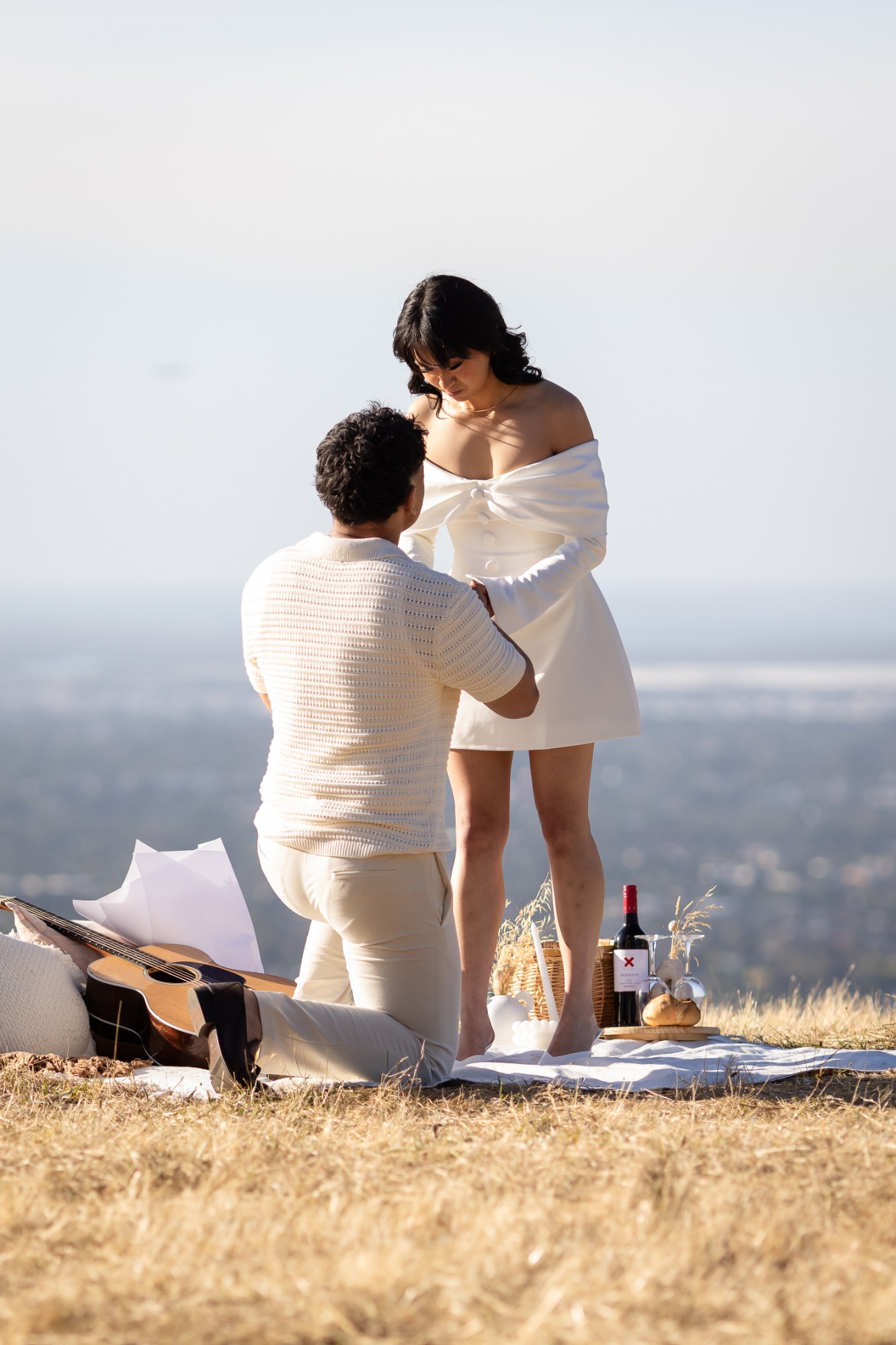 Man on one knee proposing on a picnic blanket on a golden hilltop above Adelaide