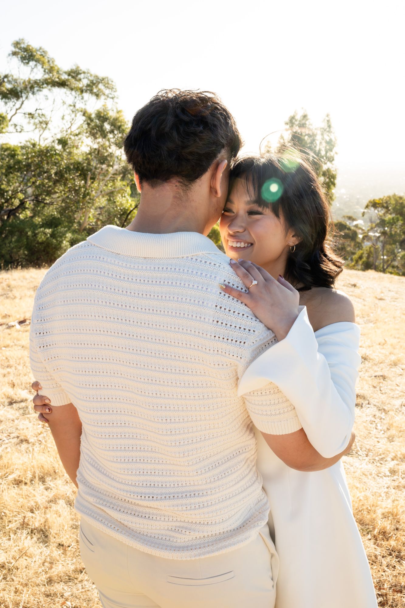 Woman smiling over her fiancé’s shoulder, her engagement ring on her hand