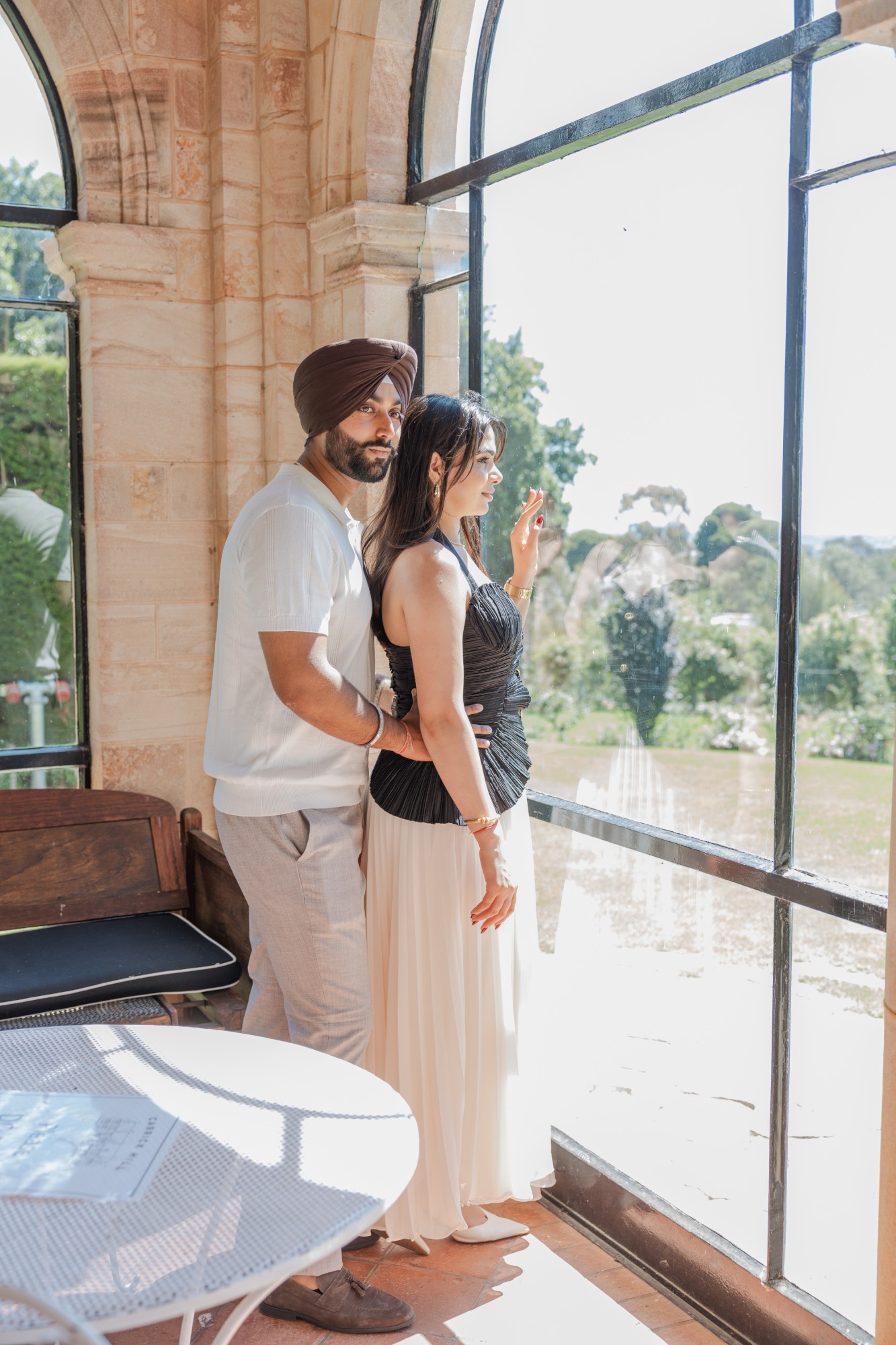 Couple at a tall arched window in a sandstone building, he holds her from behind