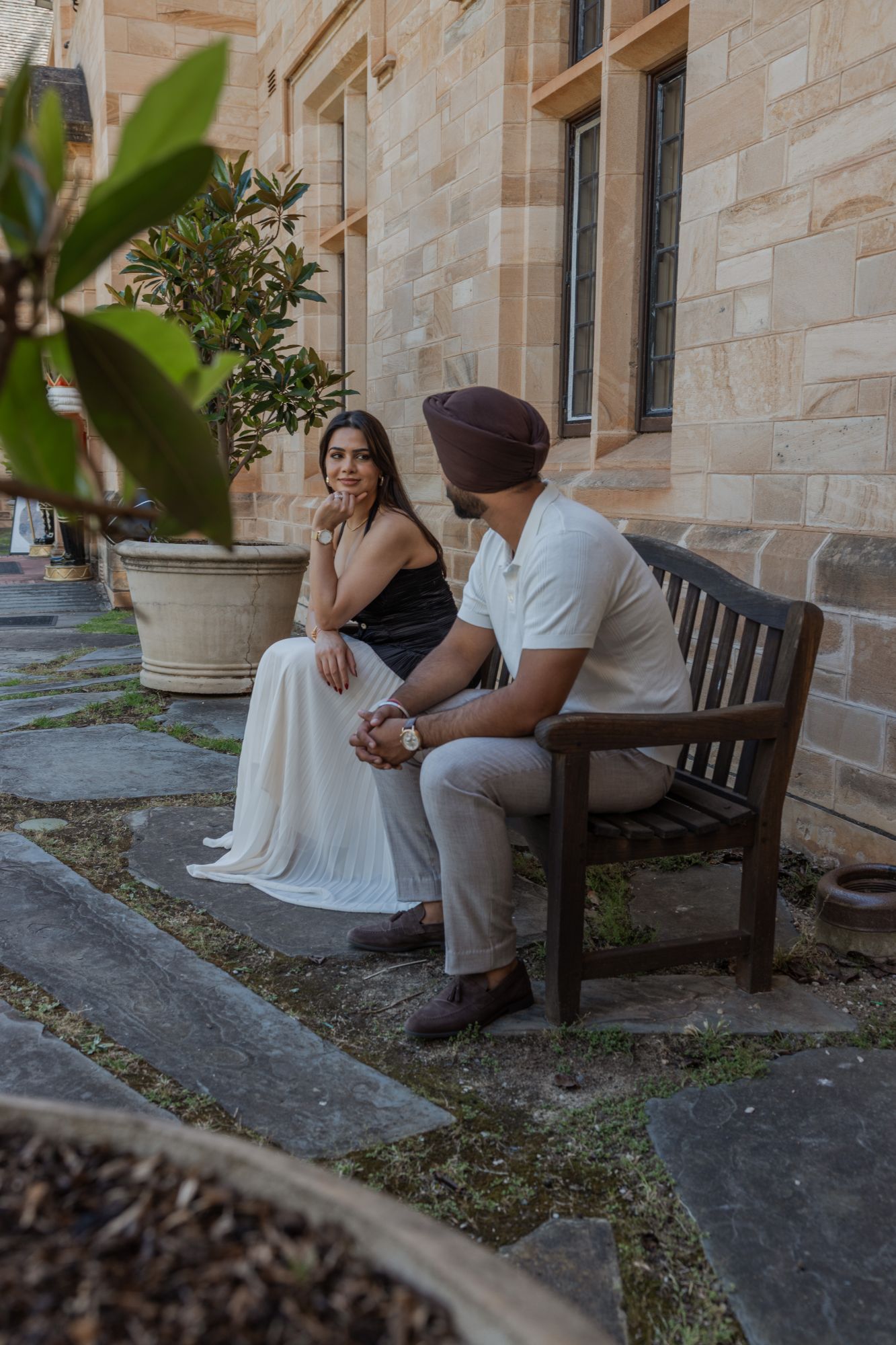 Couple on a wooden bench against a sandstone wall, smiling at each other