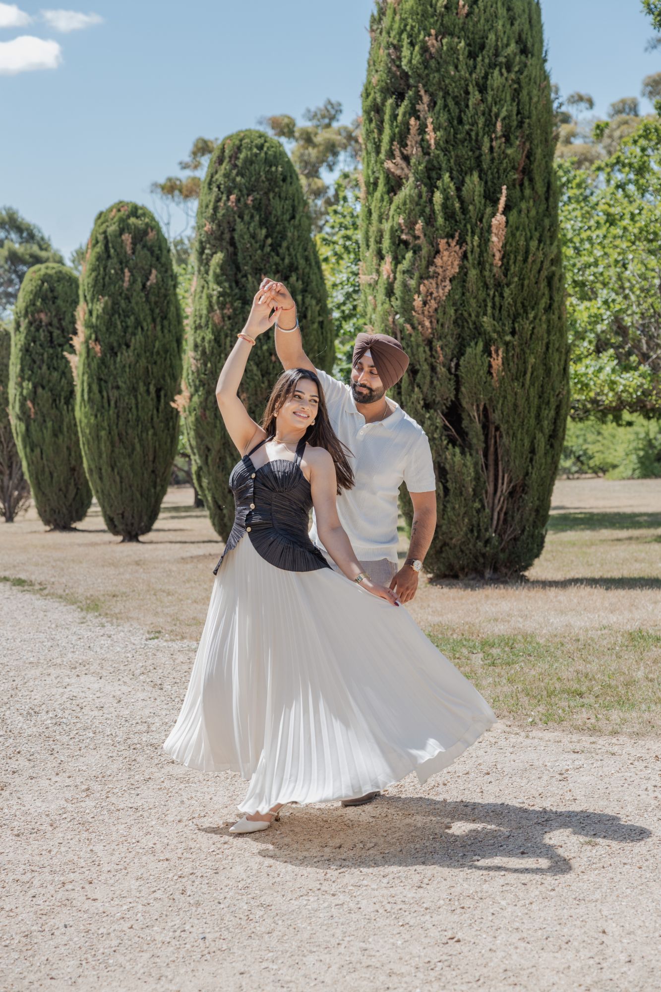 He twirls her under his arm on a gravel path lined with cypress trees