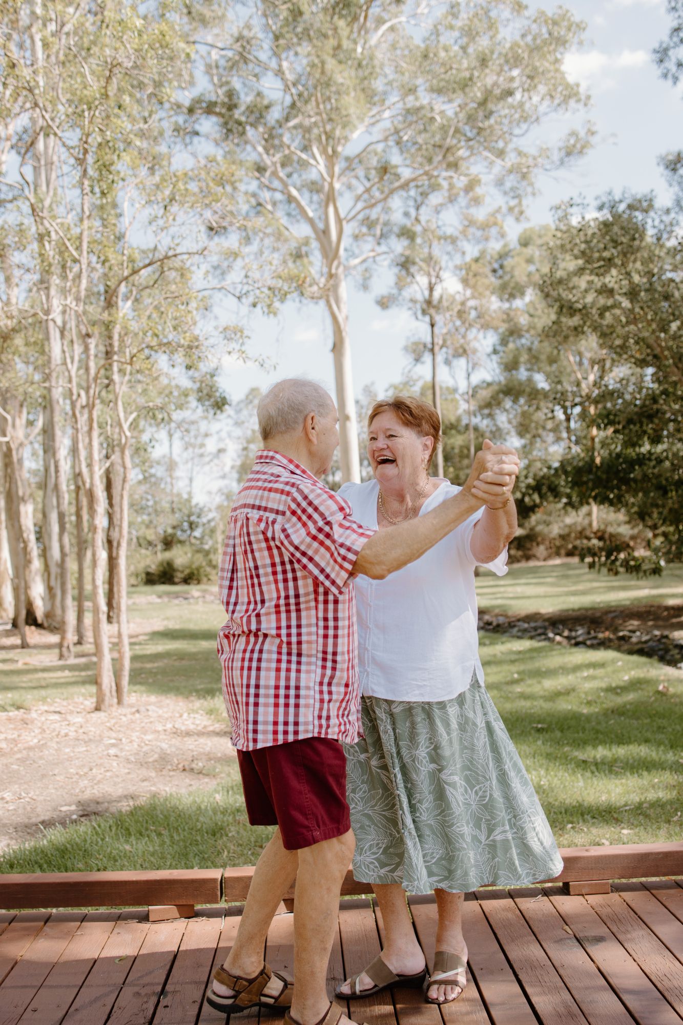 Older couple dancing on a timber boardwalk among gum trees