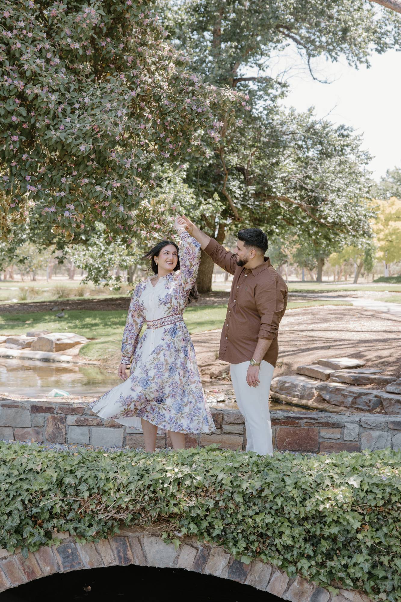 He twirls her on a little stone bridge under a flowering tree