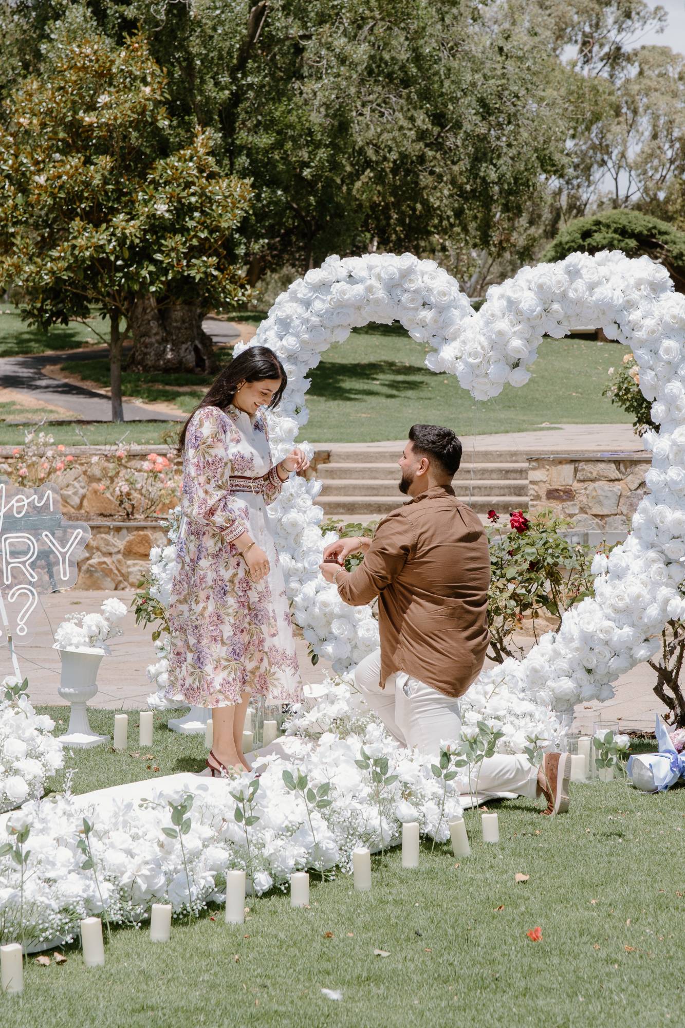 A proposal in front of a heart-shaped arch of white roses