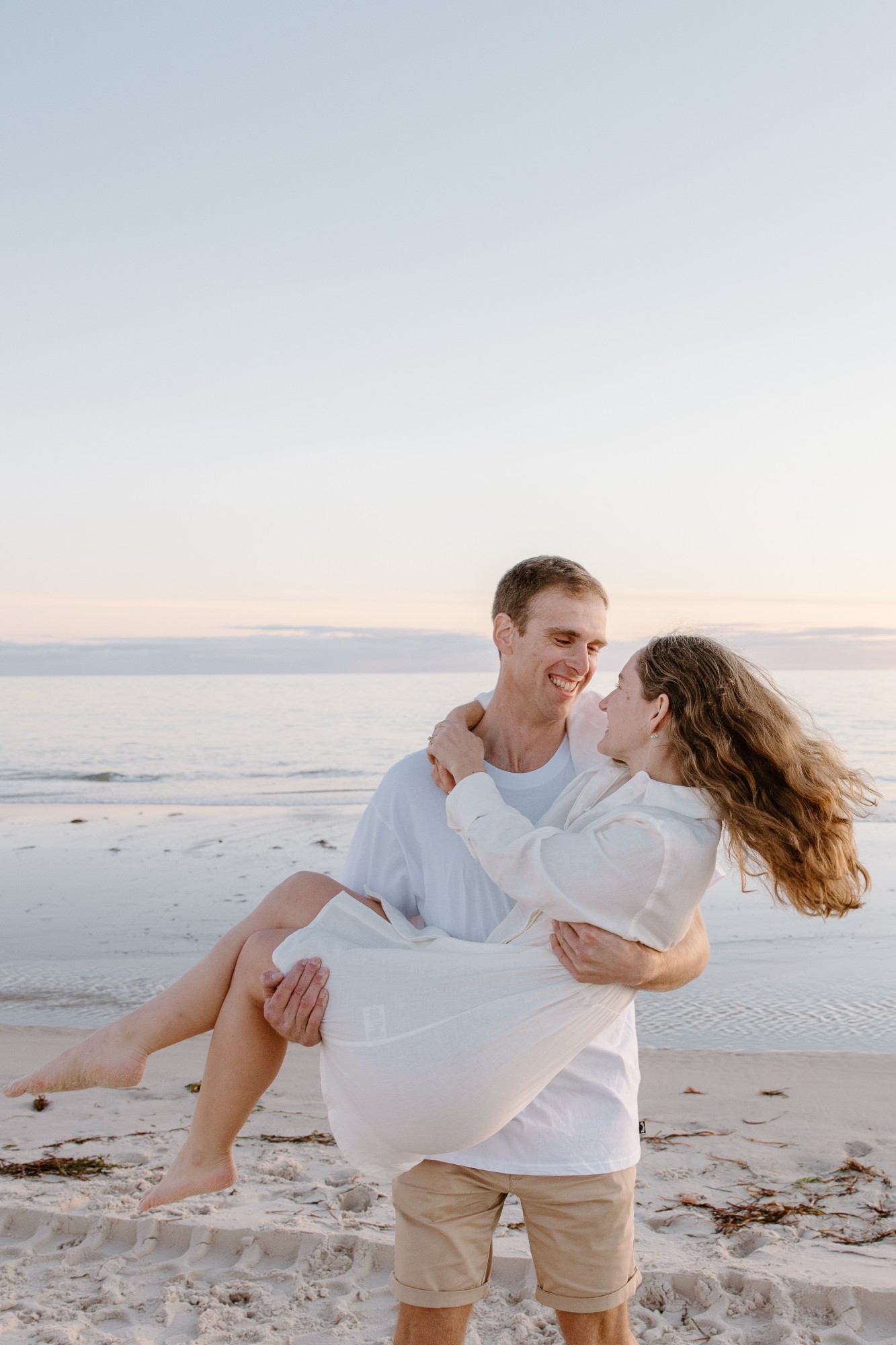He carries her along the beach, both laughing