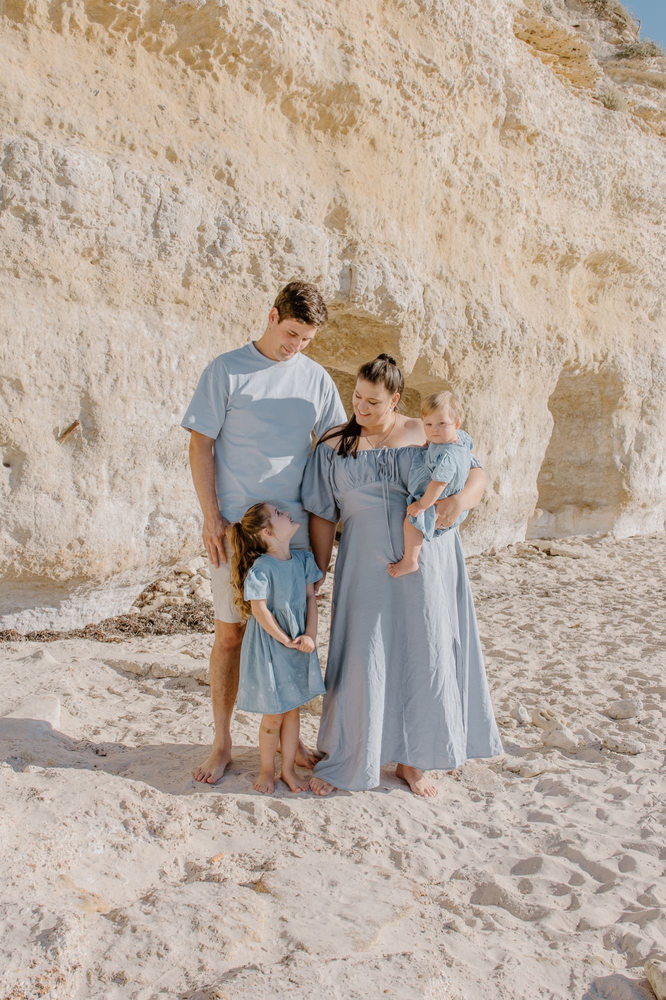 Family of four in pale blue at the foot of a limestone cliff