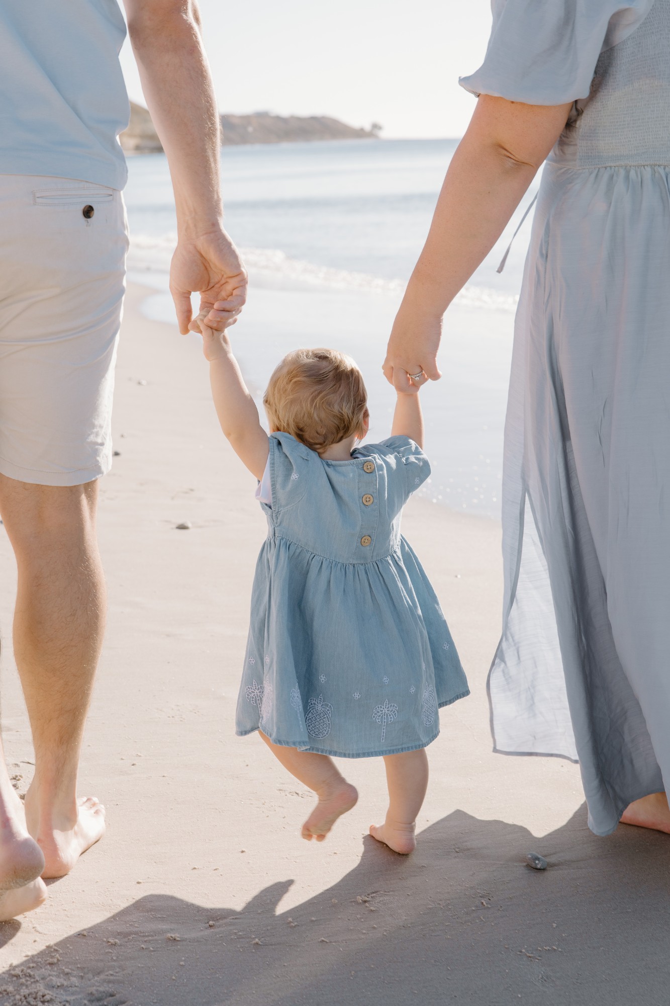 Toddler walking on the sand holding both parents’ hands
