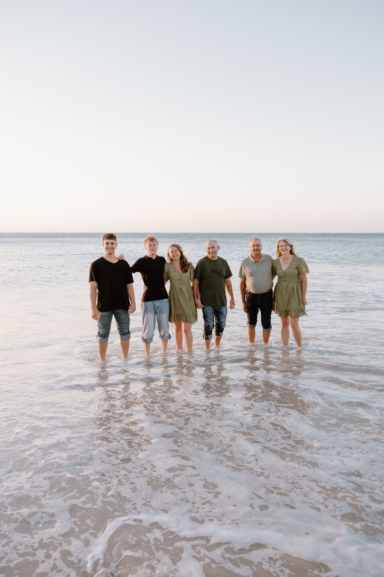 Extended family standing in the shallows at sunset