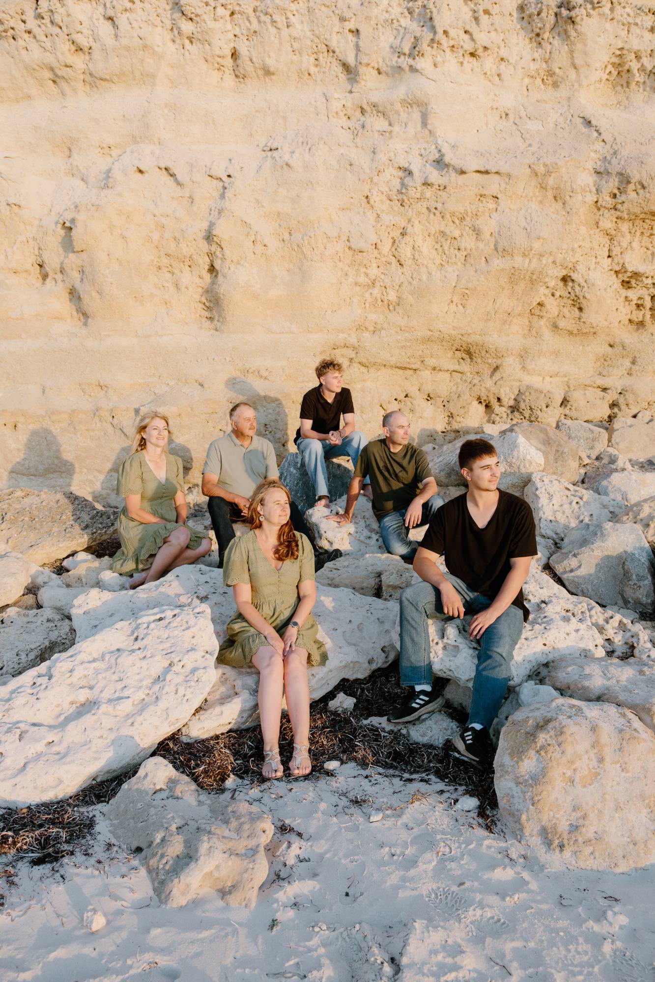 Extended family sitting on rocks below a sunlit cliff