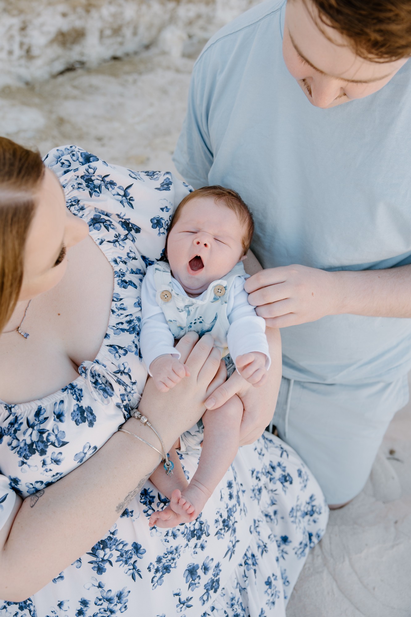Newborn yawning in his mother’s arms, his father beside them on the sand