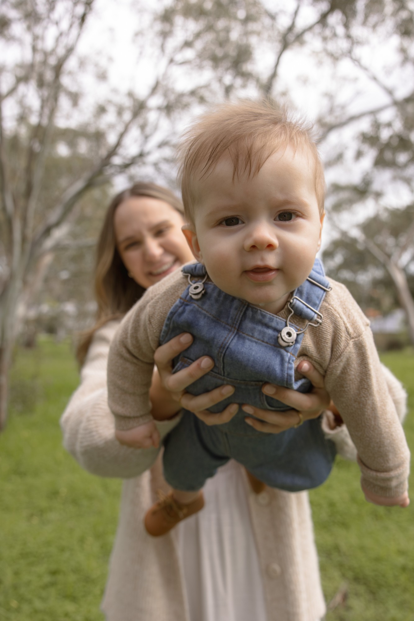 Mother lifting her baby boy towards the camera among the trees