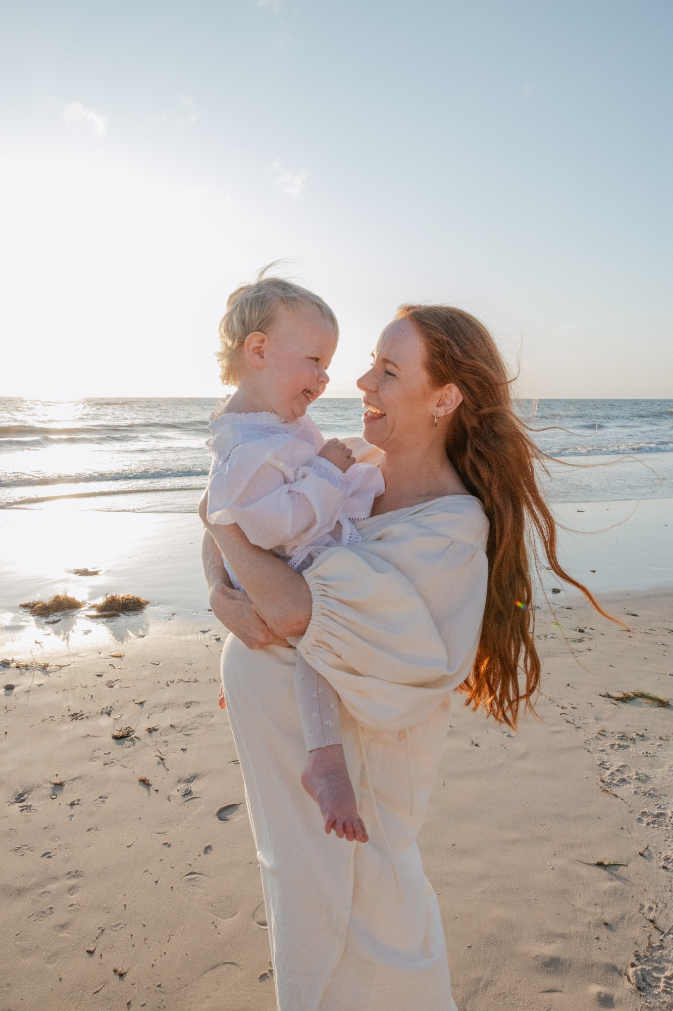 Mother holding her toddler on the beach, both laughing