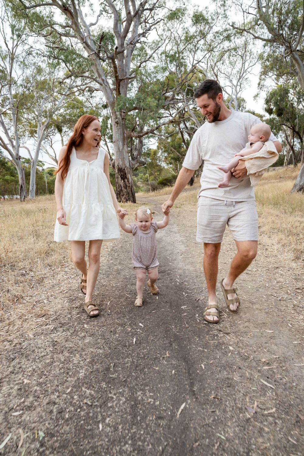 Toddler walking between her parents on a gravel track