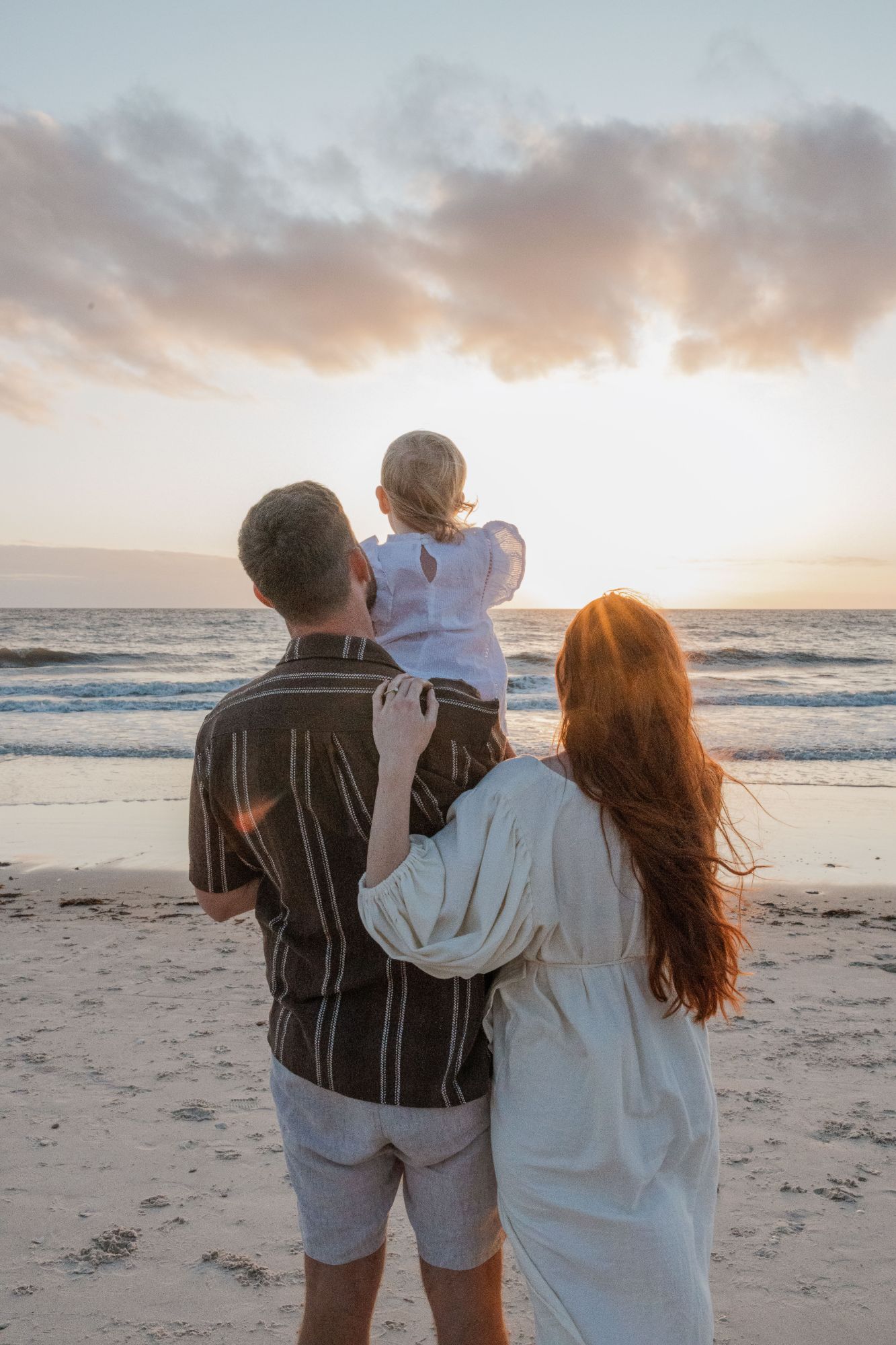 Family watching the sunset at the water’s edge, toddler on dad’s shoulders