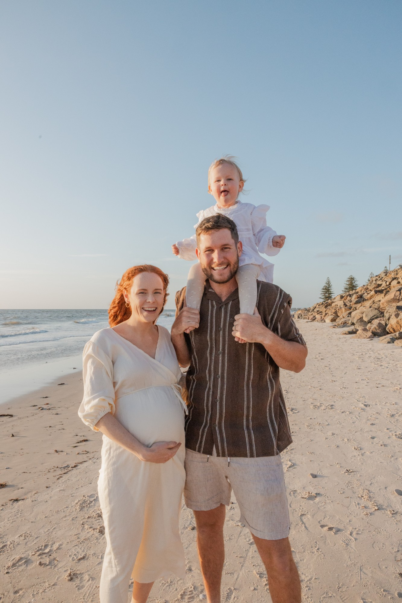 Pregnant mother and father on the beach, their toddler on his shoulders