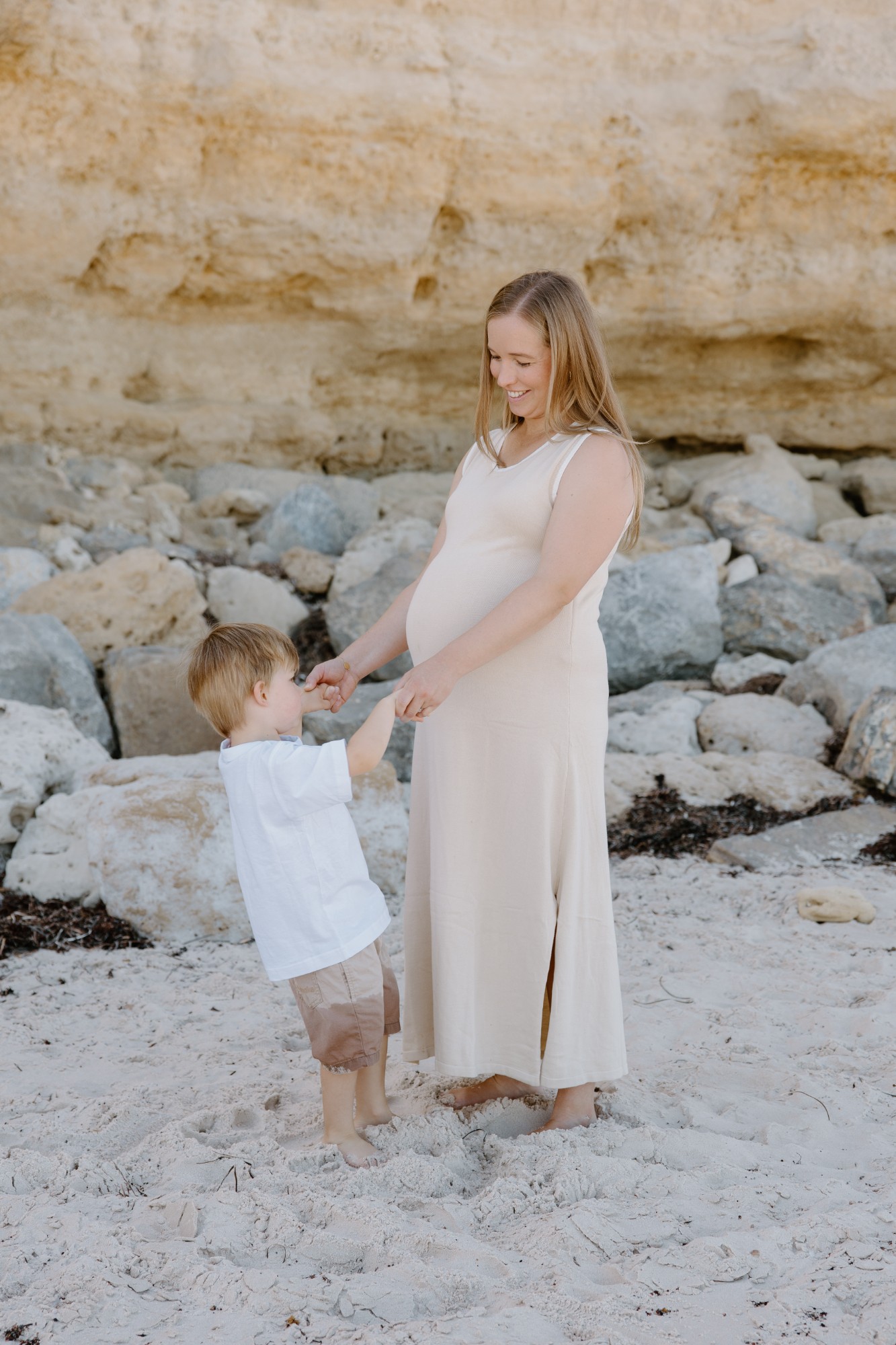 Pregnant mother holding her son’s hands on the beach below a cliff