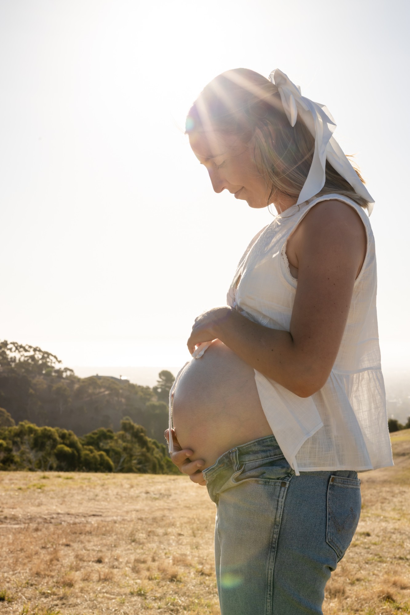 Pregnant mother looking down at her bump, the sun behind her