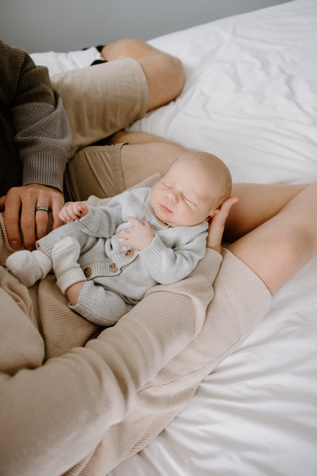 Newborn asleep across his parents’ laps on the bed