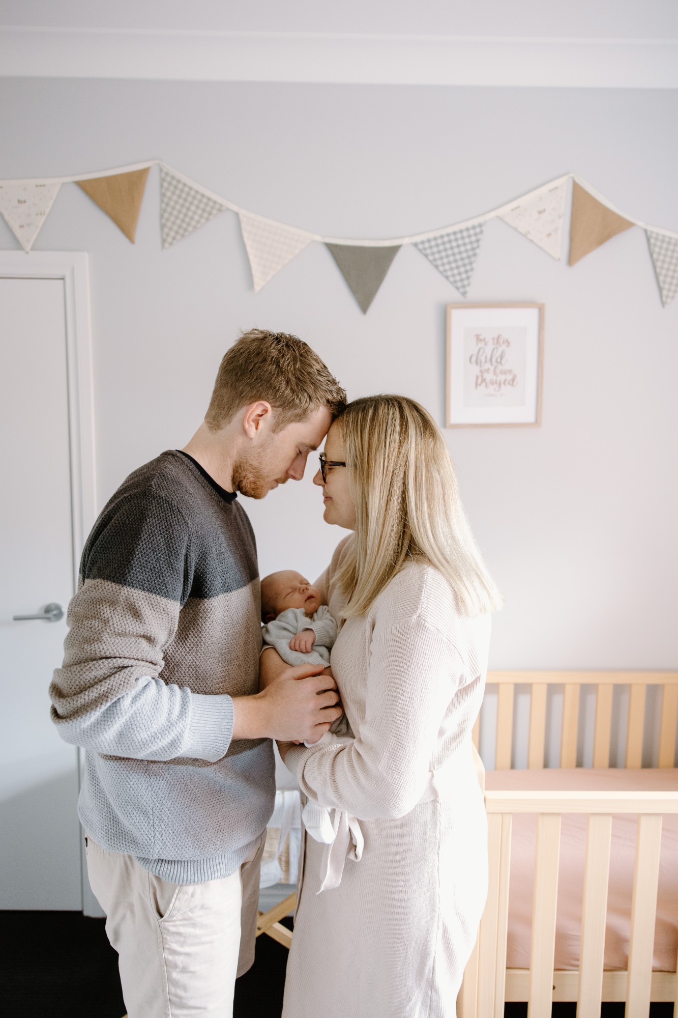 Parents forehead to forehead in the nursery, their newborn between them