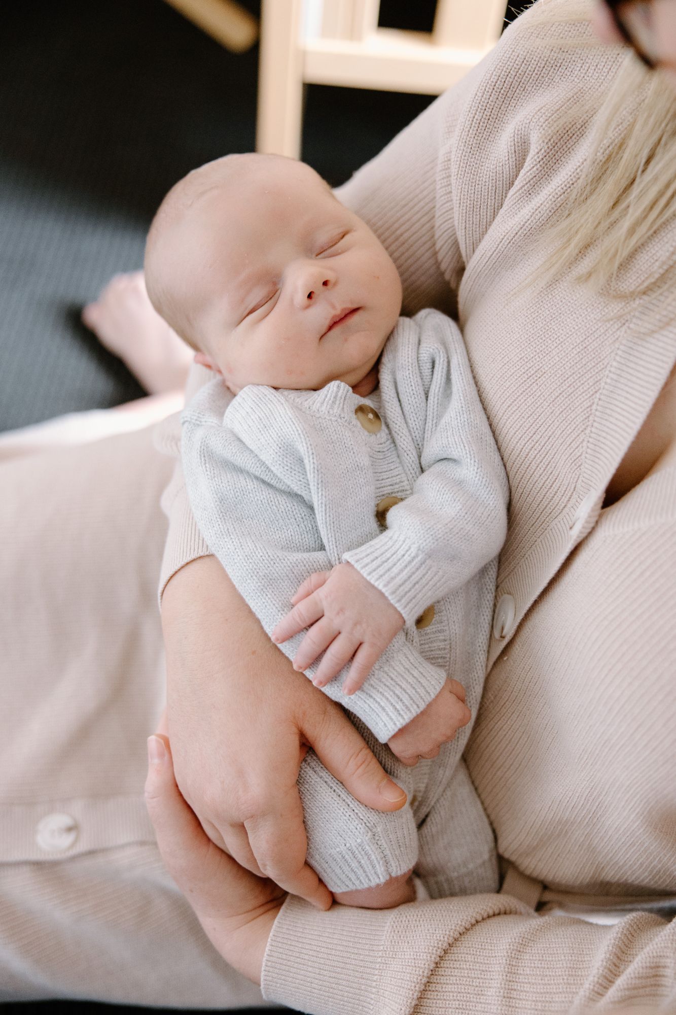 Newborn asleep in his mother’s arms in a soft knit