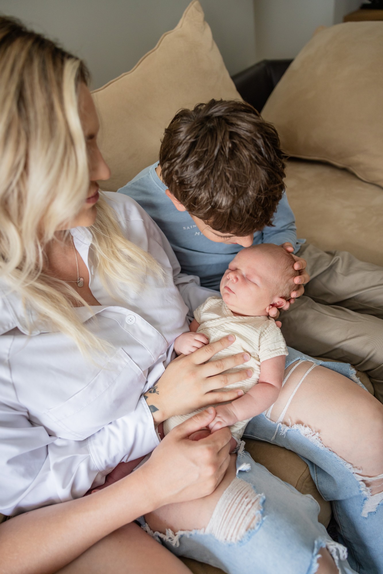 Mother and big brother leaning in over the newborn on the couch