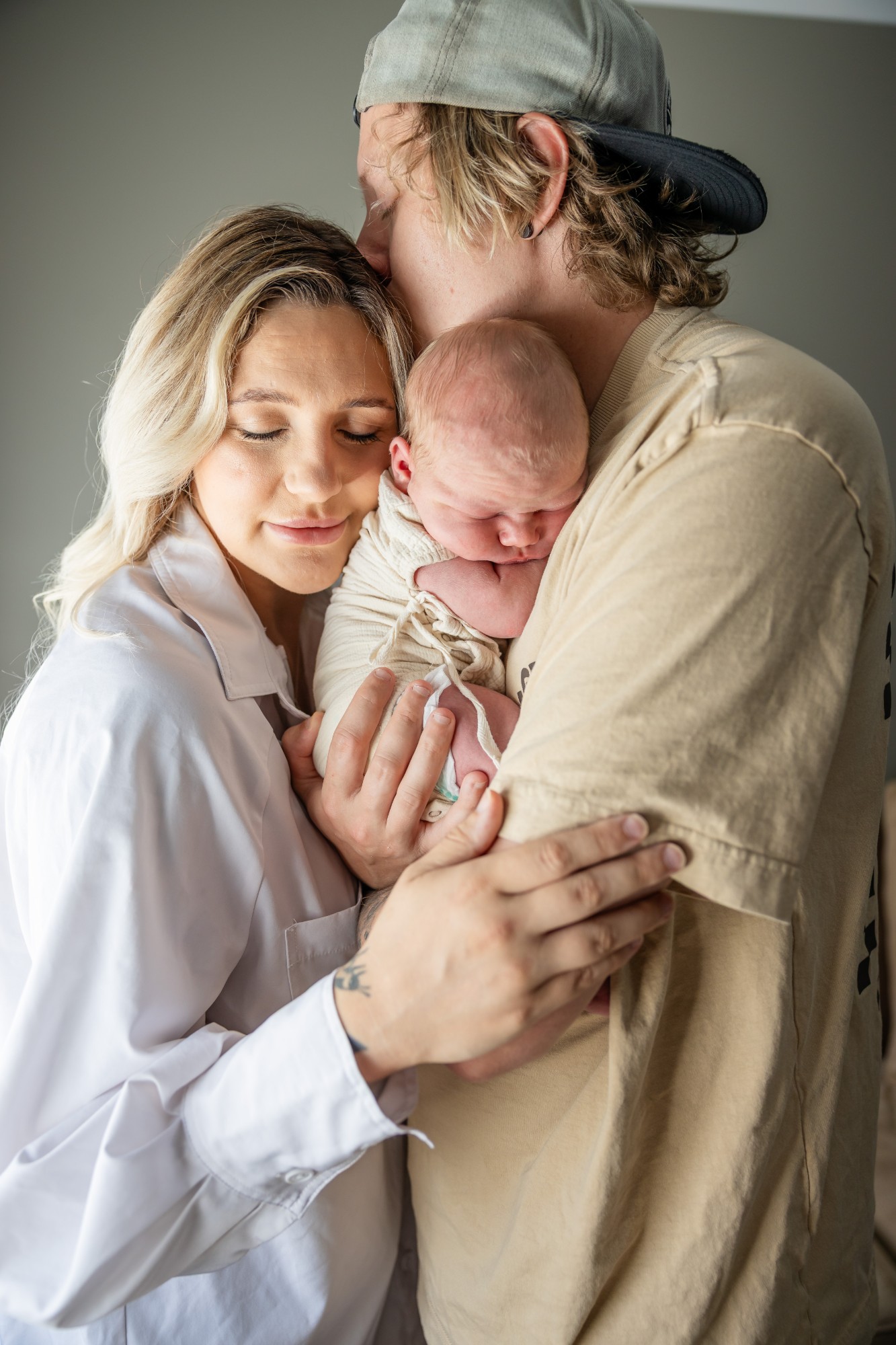 Father in a cap kissing his newborn as the mother holds him close