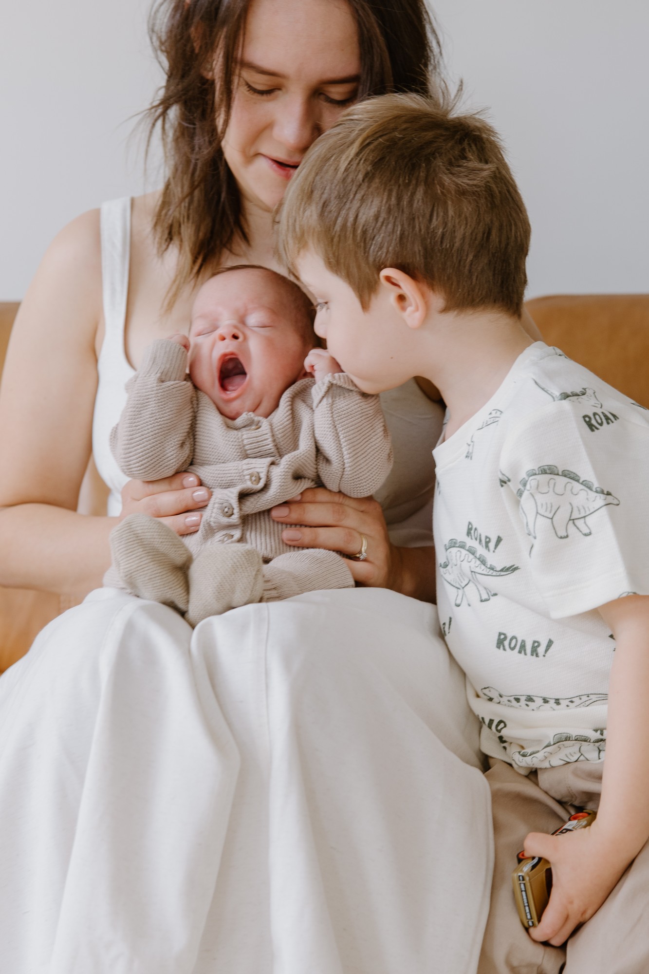 Big brother leaning in as the newborn yawns in mum’s lap