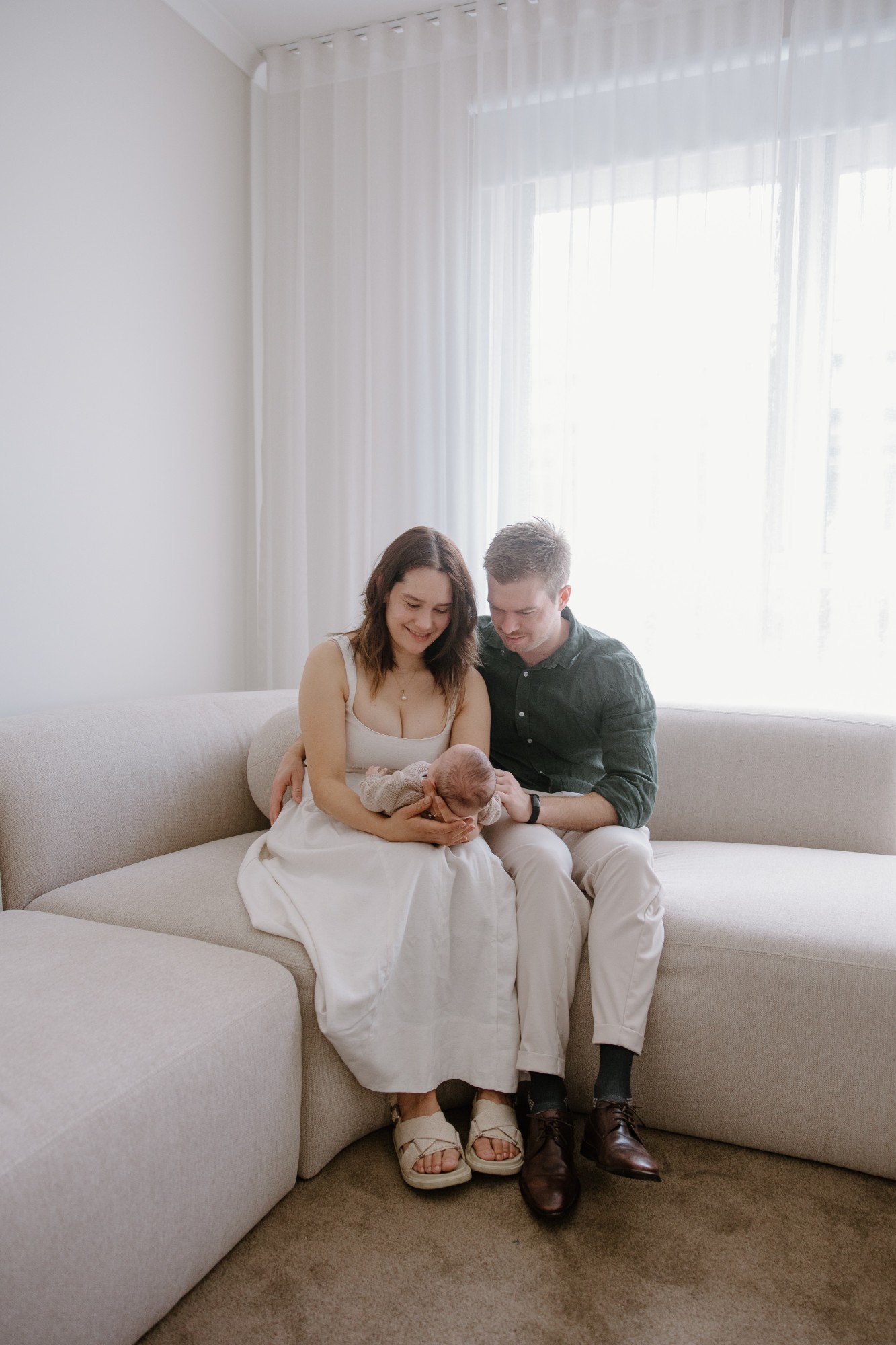 Parents on a cream sofa looking down at their newborn