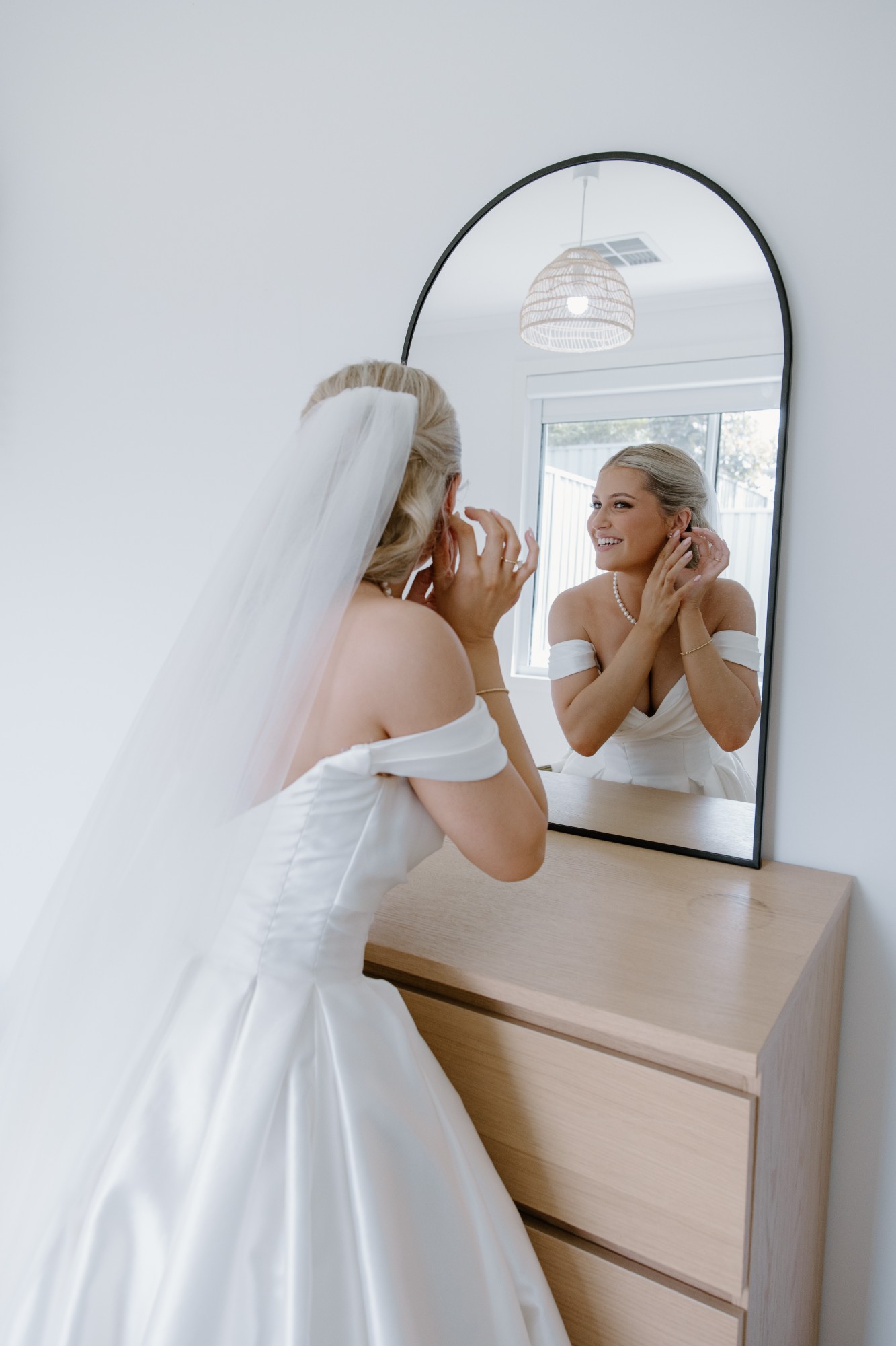 Bride putting in her earrings in an arched mirror