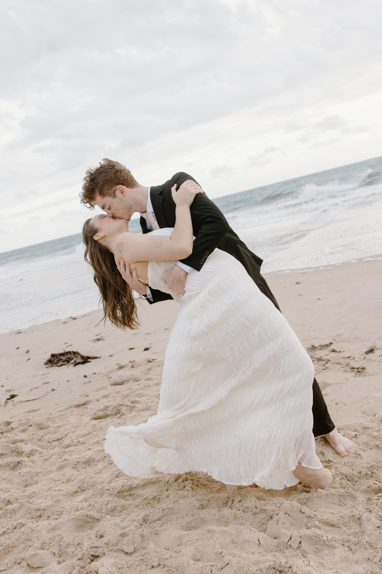 Groom dipping his bride on a windy beach