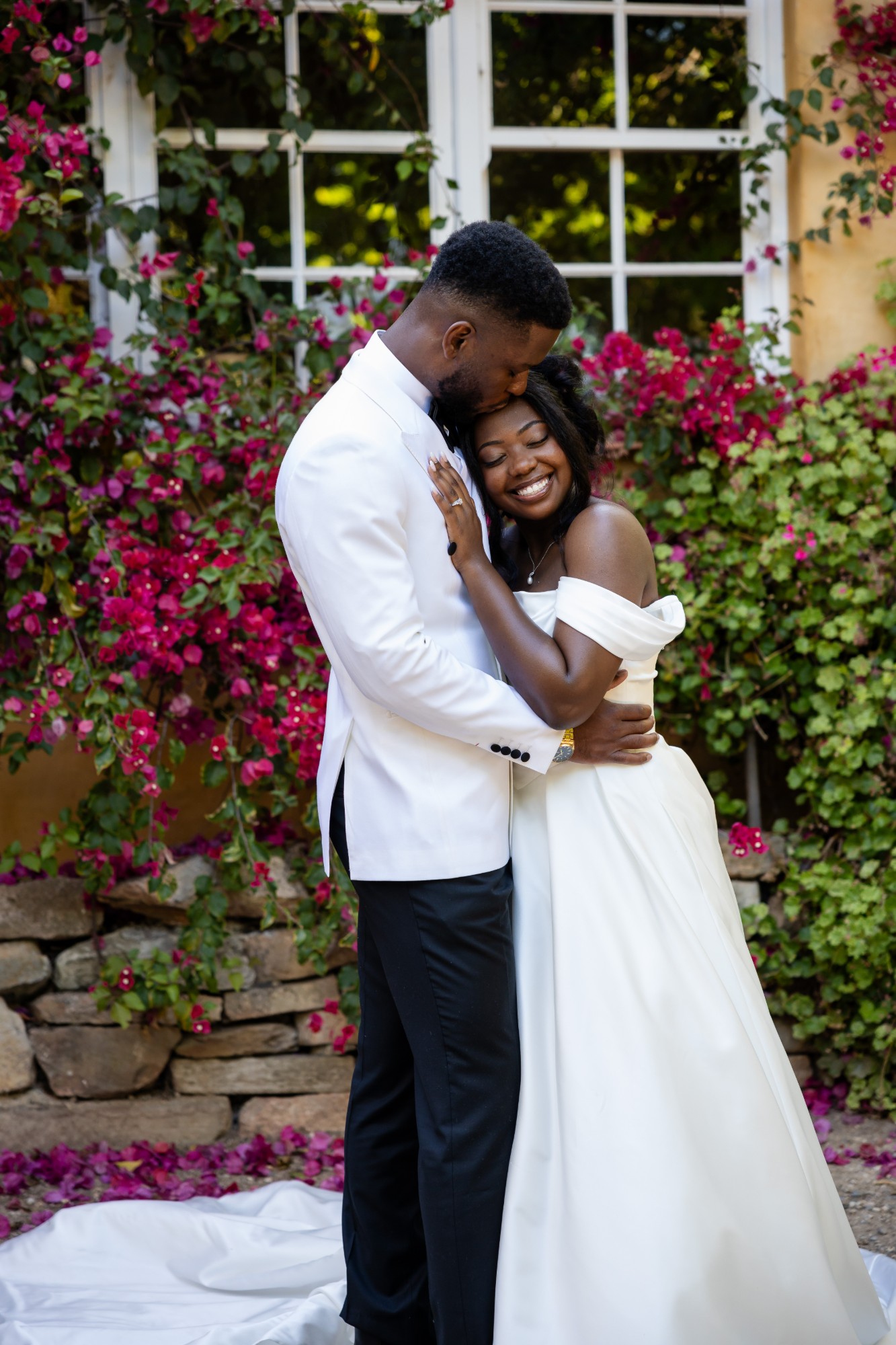 Groom kissing the bride’s forehead in front of bougainvillea