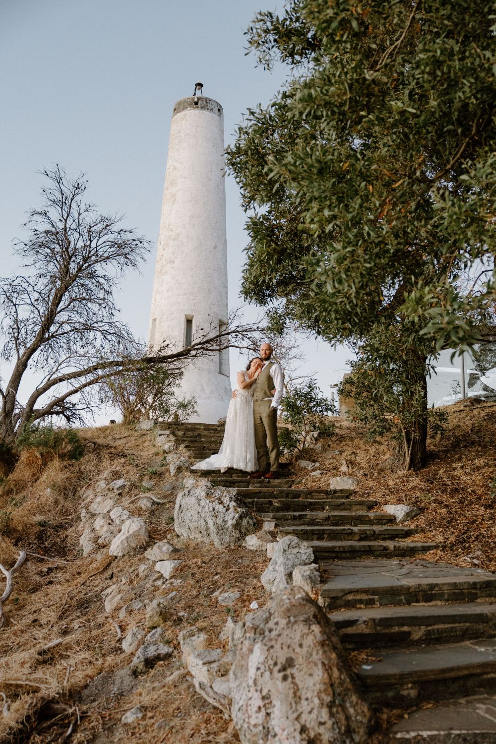 Bride and groom on stone steps below a white lighthouse