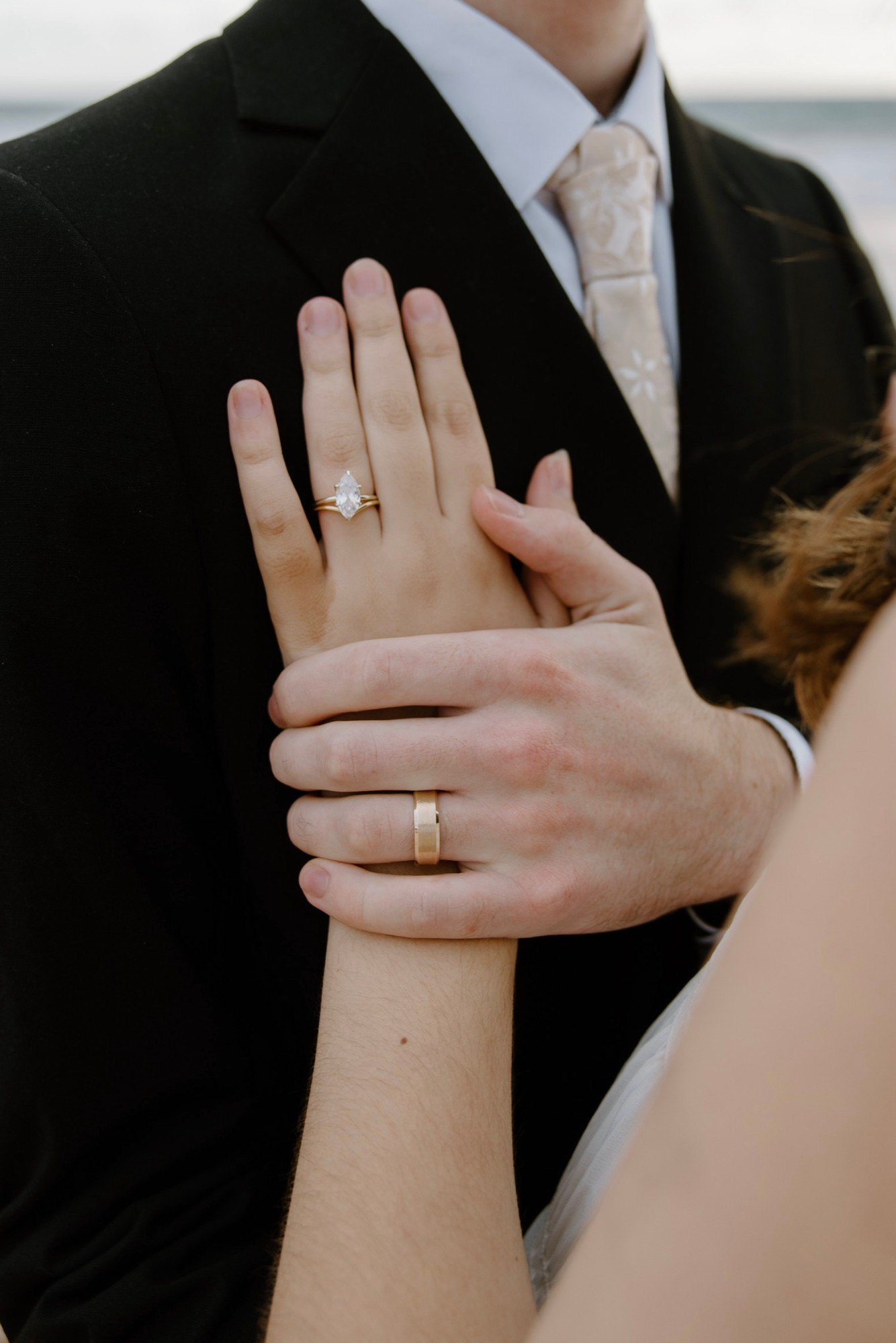 The bride’s hand with her rings on the groom’s chest, his hand over hers