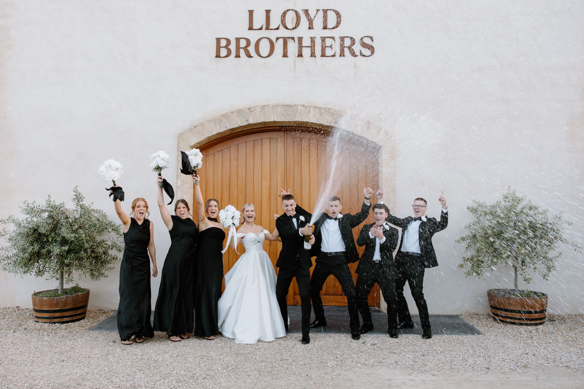 Bridal party cheering as the groom sprays champagne outside the Lloyd Brothers winery doors